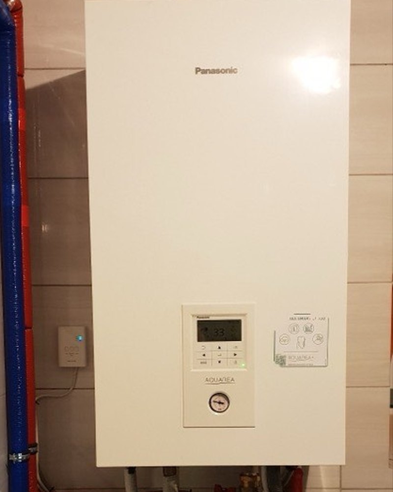 Hydromoduł pompy ciepła Panasonic Aquarea na ścianie w kotłowni, sterownik wskazuje 33°C — realizacja Instal-Home