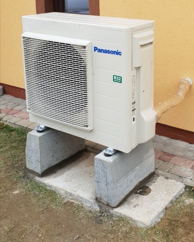 Jednostka zewnętrzna klimatyzacji Panasonic R32 na bloczkach przy żółtej elewacji domu — montaż Instal-Home